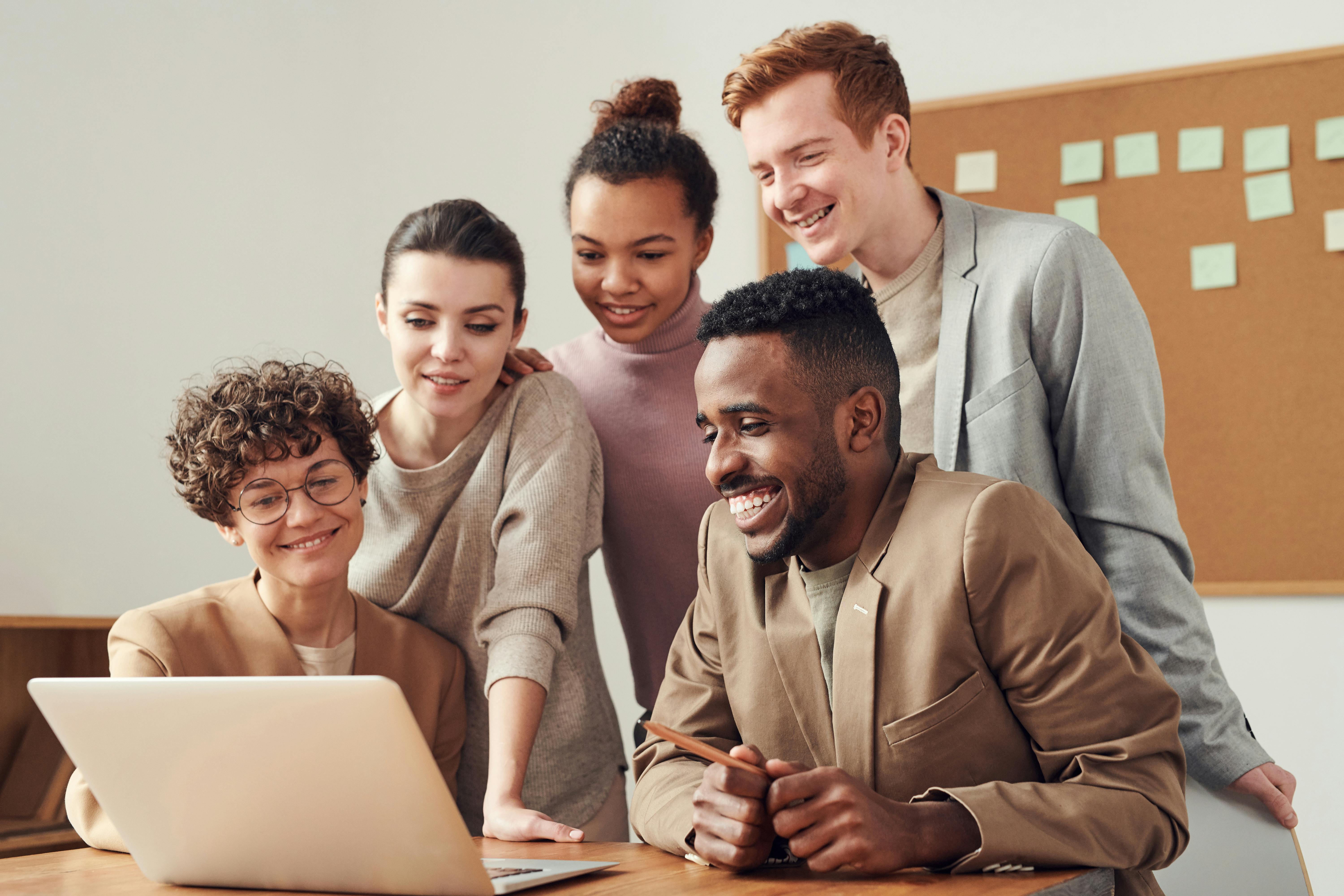 A group of people smiling around a laptop